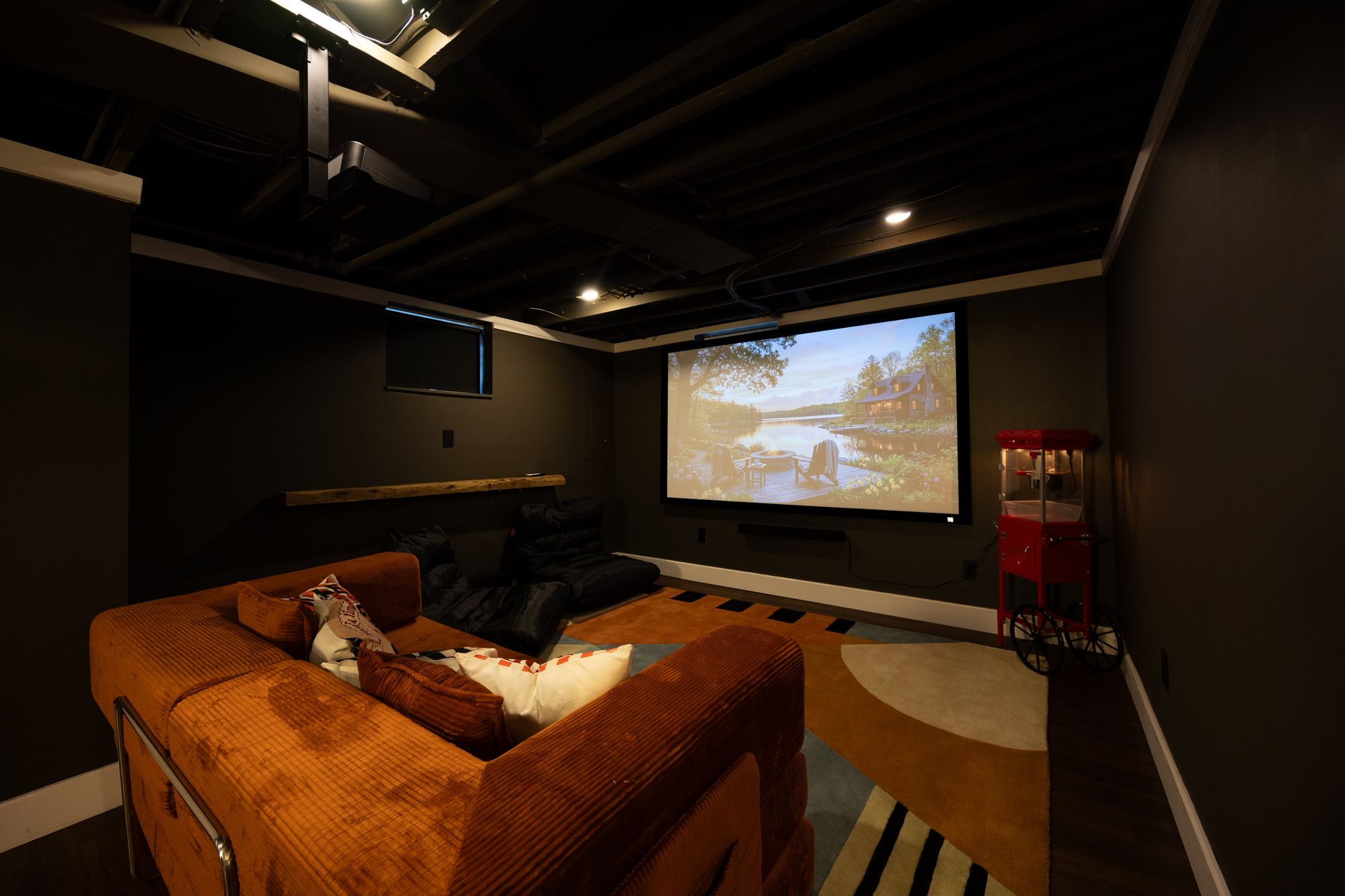 Basement cinema with orange sectional, projector screen and popcorn cart